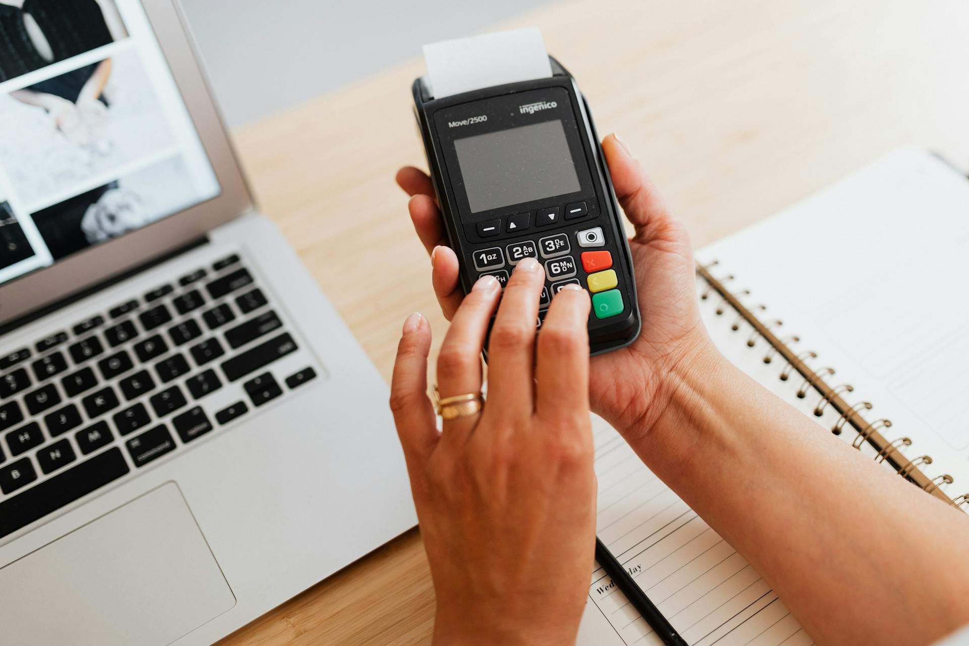 Hands using a payment terminal next to a laptop and notebook, showcasing cashless transactions.