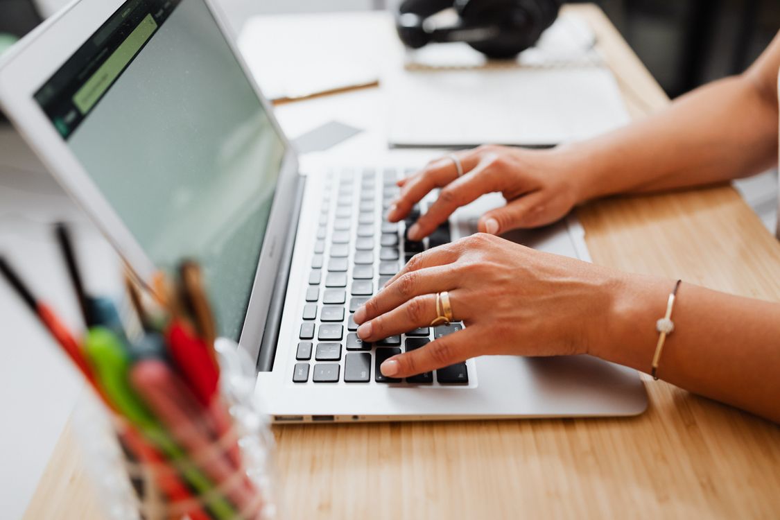 Hands typing a first draft on a laptop at a wooden desk, the starting point of an AI content creation workflow