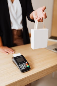 Close-up of shopper's hand holding a bag next to a payment terminal on a wooden counter.