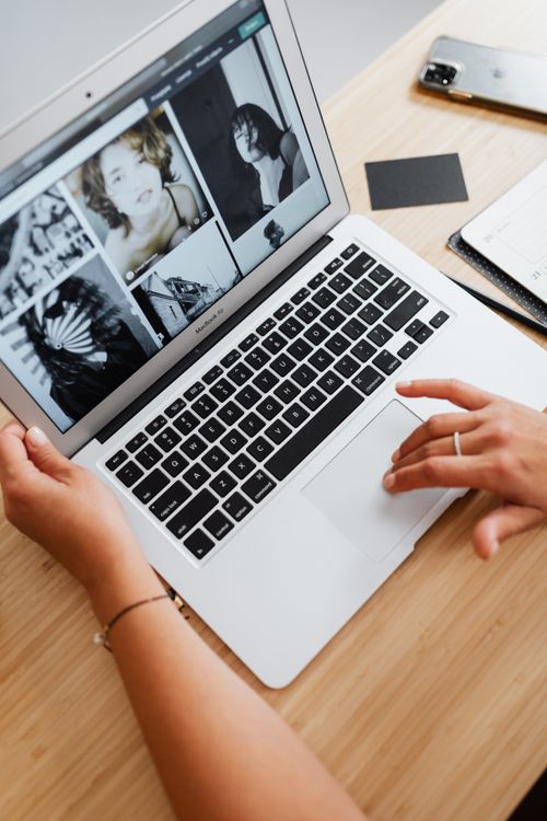 Free Hands on laptop browsing photos, wooden desk setup. Perfect for depicting digital workspace themes. Stock Photo
