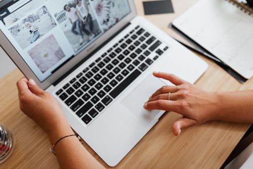Free Close-up of hands browsing photos on a laptop at a wooden desk, showcasing internet browsing at work. Stock Photo