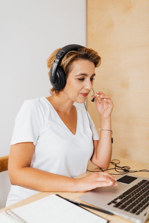 Free Woman in White V Neck T-shirt Wearing a Headset while in Front of the Laptop Stock Photo