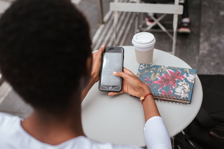 Unrecognizable Black Woman Messaging On Phone At Cafe