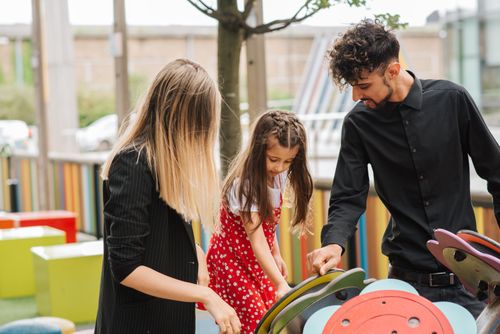 Free Little girl playing on playground with support of mother and father in casual clothes in summer day Stock Photo