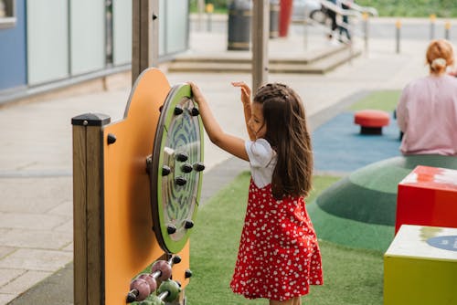 Side view of little girl playing with toy on playground in casual outfit in daytime on street