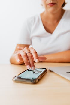 Close-up of a woman operating a smartphone at a wooden desk with a laptop, showcasing modern technology use.