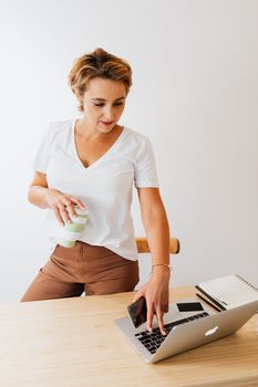 Modern office scene with a woman using a laptop and smartphone, holding a reusable coffee cup.