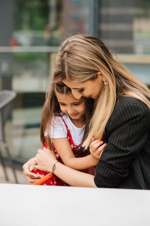 Free Adult lady embracing little girl while sitting on street in casual clothes in sunny day Stock Photo