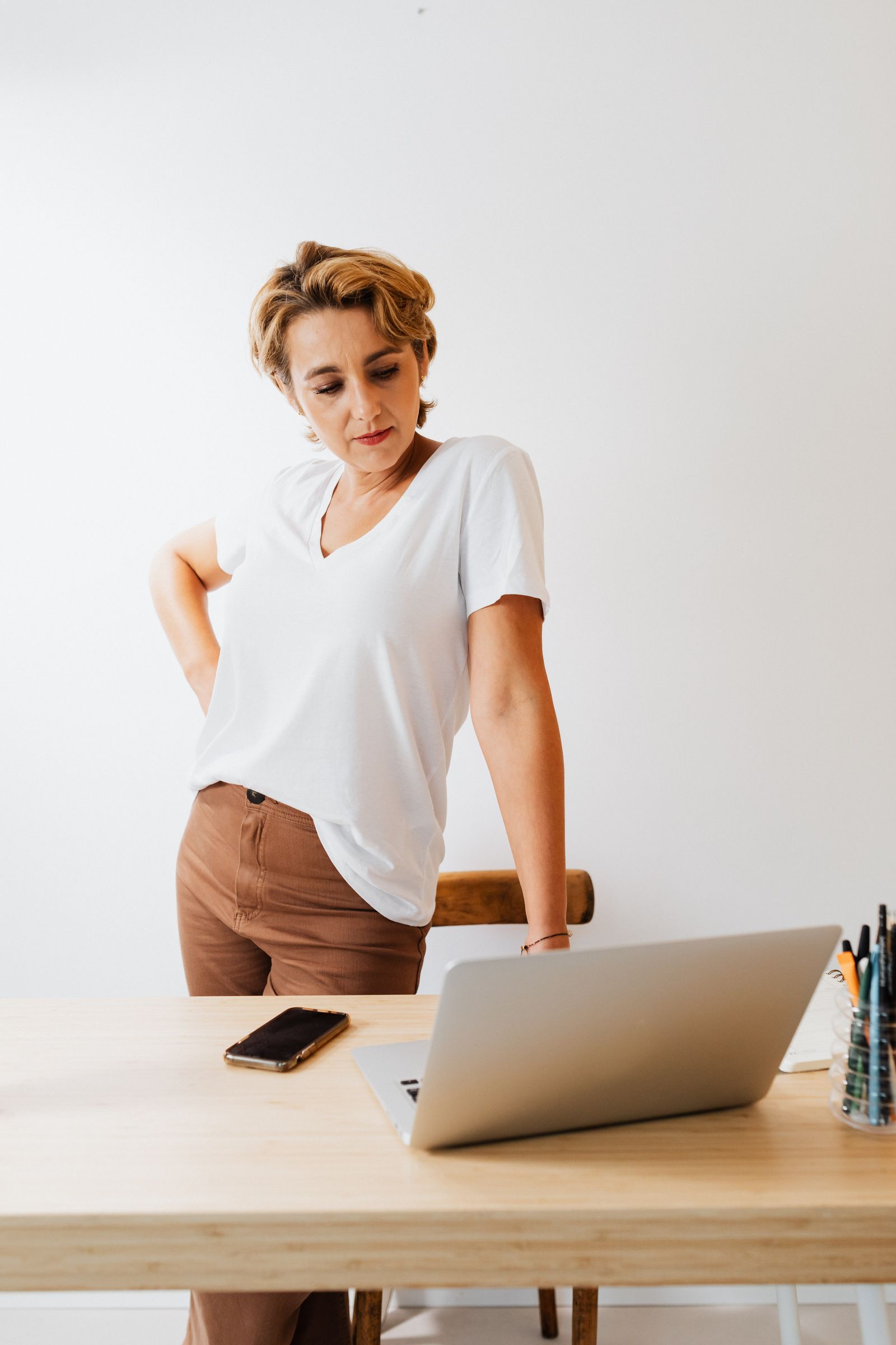 Woman standing at a desk looking down at a laptop with rounded shoulders from computer work