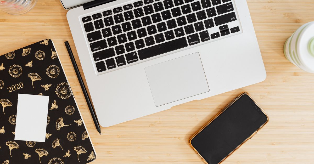 A simple notebook and pen next to a flip phone on a wooden desk, suggesting a minimalist, intentional lifestyle