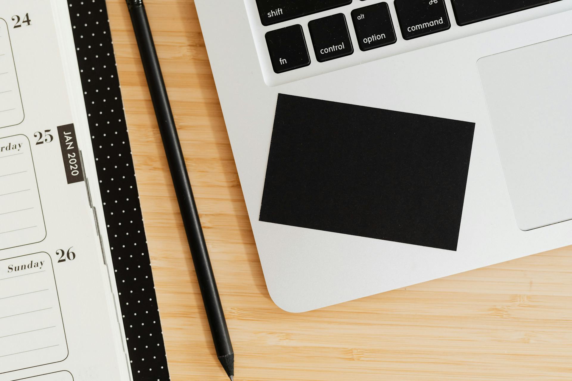 A clean office desk setup with a laptop, notebook, pen, and business card on a wooden surface.