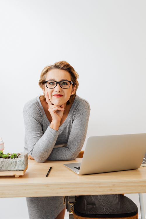 Free Smiling woman sitting at desk with laptop and plants, ideal for modern office settings. Stock Photo