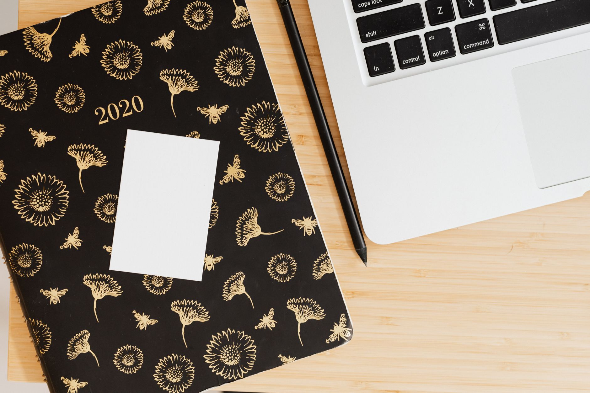 Top view of a modern workspace featuring a floral planner, pen, and laptop on a wooden desk.
