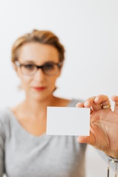 A professional woman holds a blank business card against a blurred background.