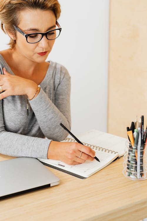 Woman Sitting at the Desk and Writing in a Notebook