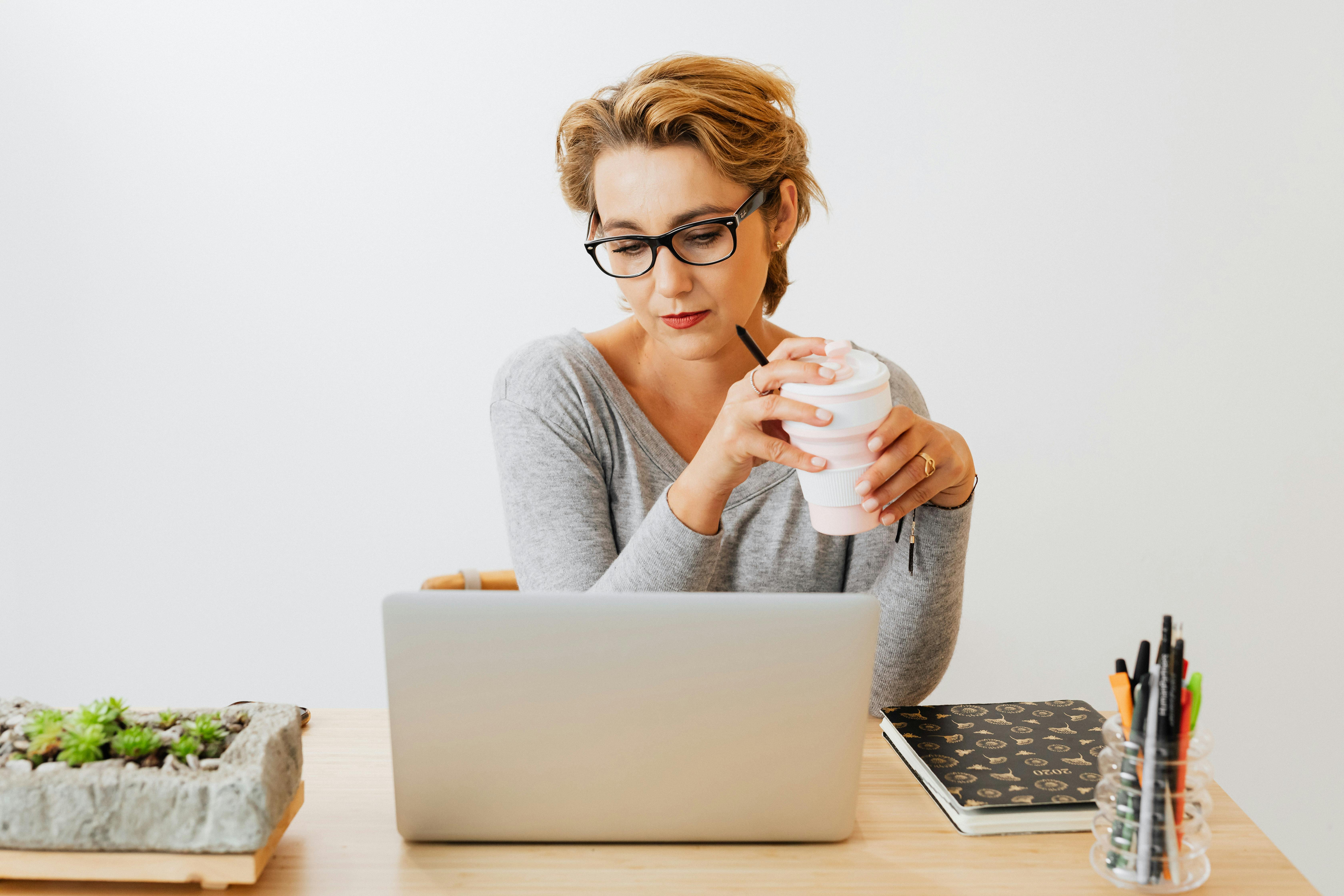 在办公室环境中，一位专注的女性拿着咖啡杯，用笔记本电脑工作