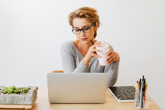 在办公室环境中，一位专注的女性拿着咖啡杯，用笔记本电脑工作