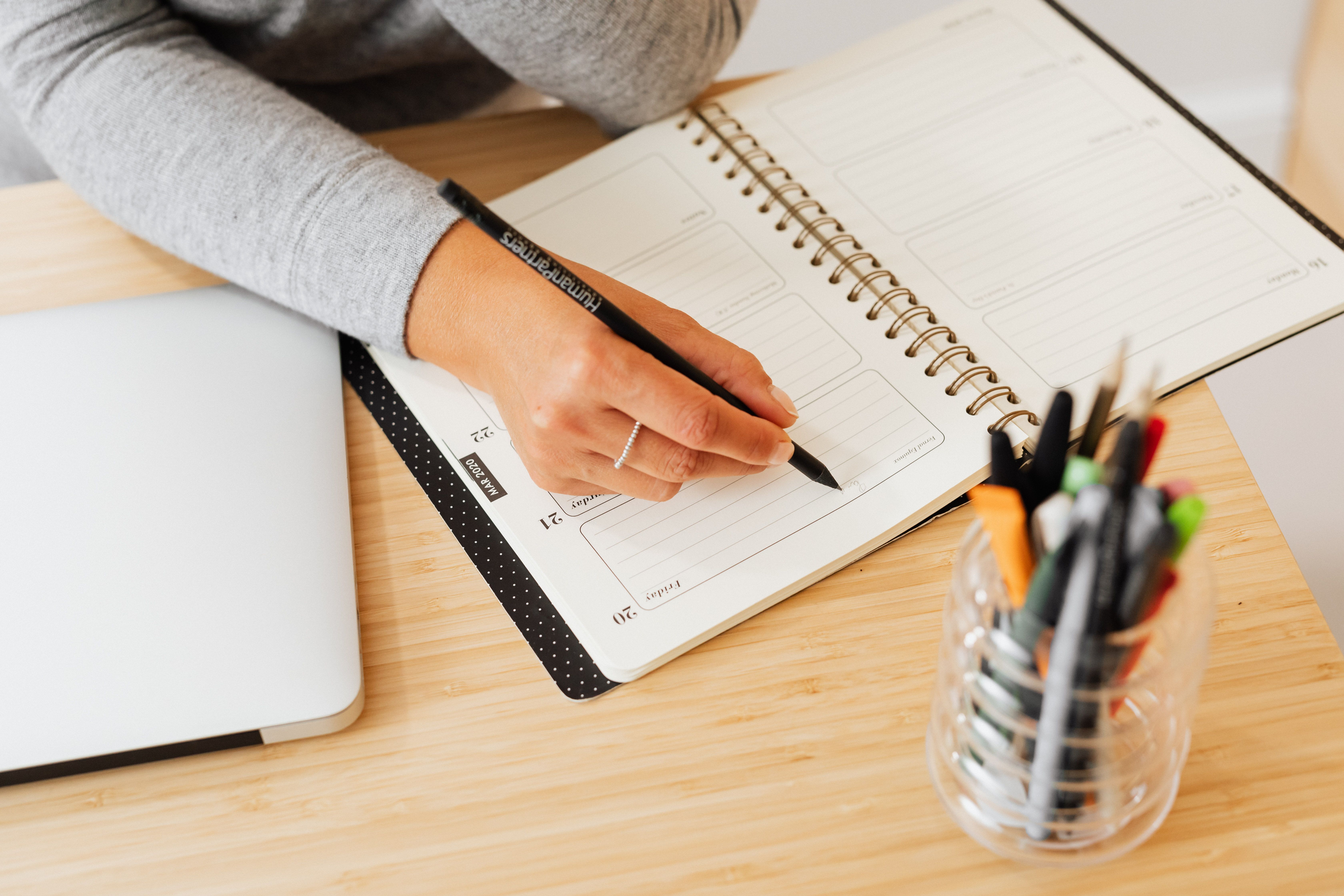 A person writing notes in a planner at a desk, representing the habit of tracking referral outcomes to sustain reciprocity