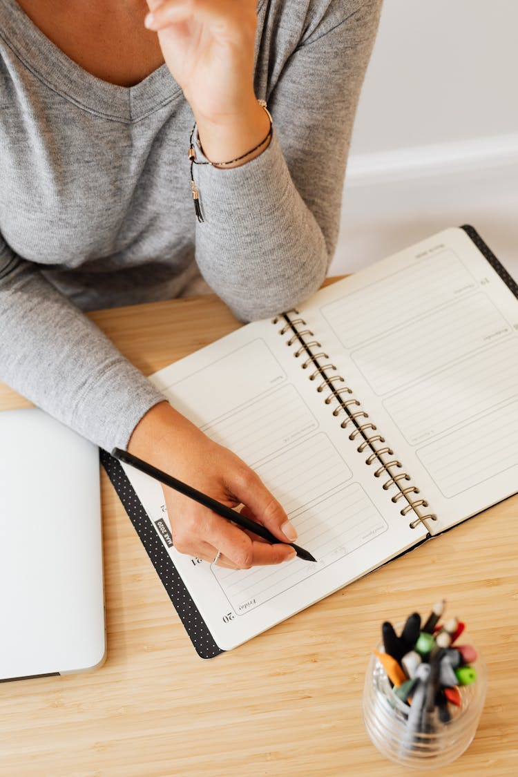 A Person Writing On A Notebook