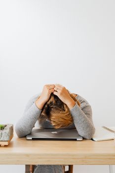 一名身穿灰色长袖的女子将头靠在笔记本电脑上，显得疲惫不堪
