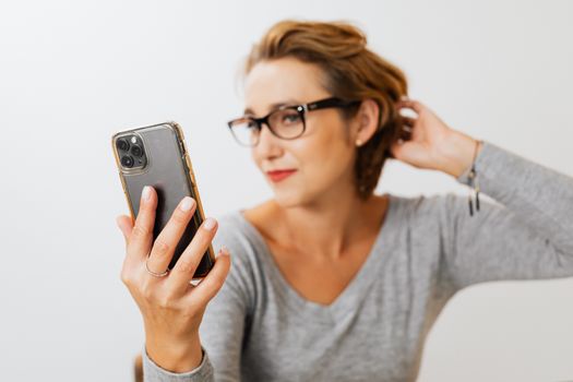 一位自信的女人戴着眼镜，拿着智能手机，在室内整理头发