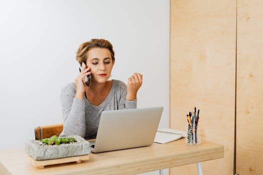 Focused woman using a laptop and mobile phone in a modern workspace.