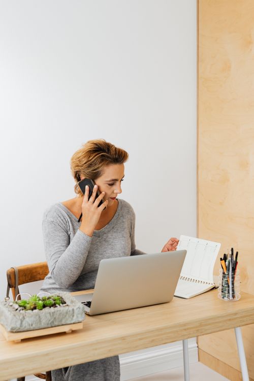 Free Businesswoman multitasking with laptop and phone in modern home office. Stock Photo