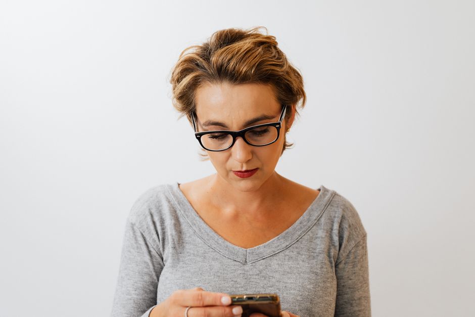 Elegant business woman with eyeglasses using a smartphone indoors, focused and stylish.