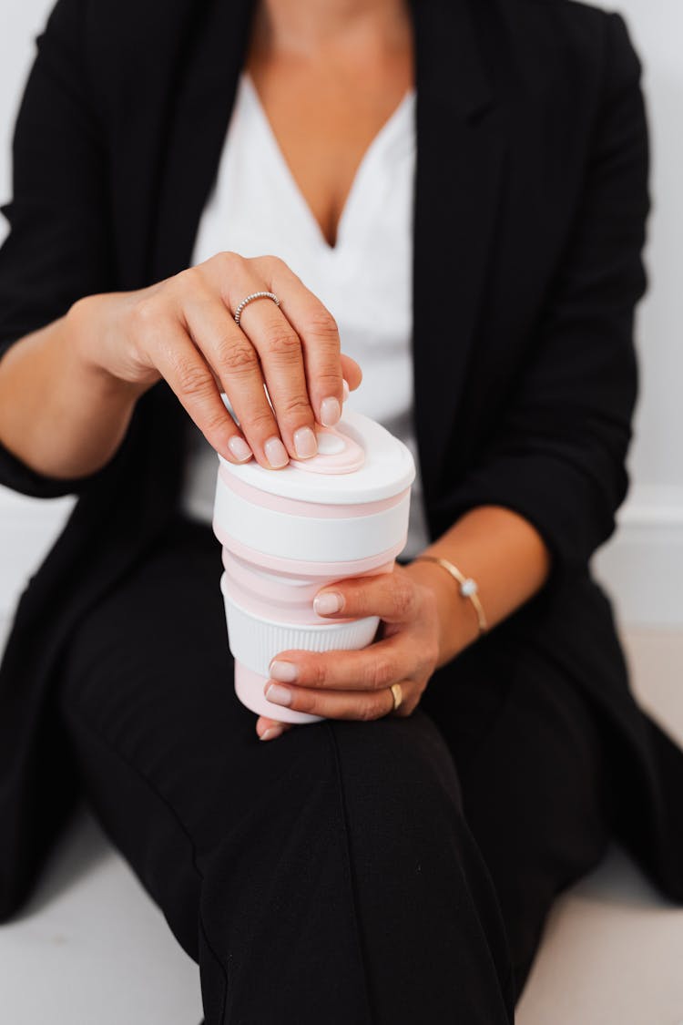 Person In Business Attire Removing The Cover Of The Collapsible Cup She Is Holding