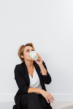 Female professional in black blazer sipping from a collapsible cup, seated and smiling.