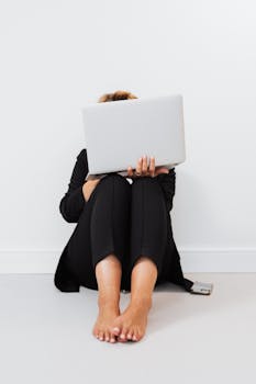 A woman sits barefoot on the floor using a laptop, symbolizing relaxed remote work.