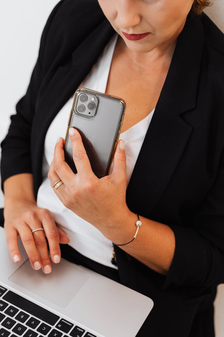 Woman Holding A Phone While Using A Laptop