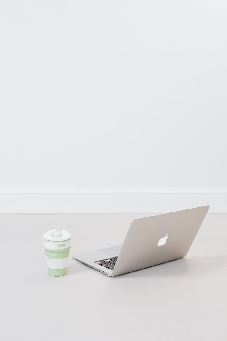 A MacBook And Silicon Cup On The Floor
