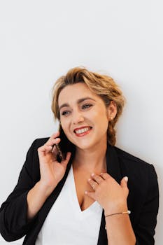 A smiling woman in a black blazer talks on the phone indoors. Perfect for business contexts.