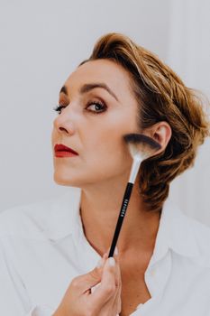 A sophisticated woman applying makeup with a brush, showcasing elegant beauty and cosmetic application.