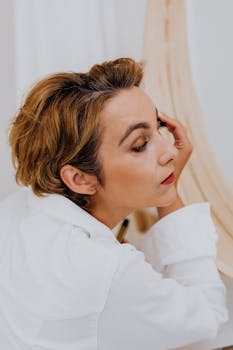 Adult woman applying makeup with focus and elegance in a minimalist indoor setting.