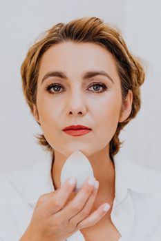 Close-up portrait of a woman using a makeup sponge, showcasing elegance and beauty.