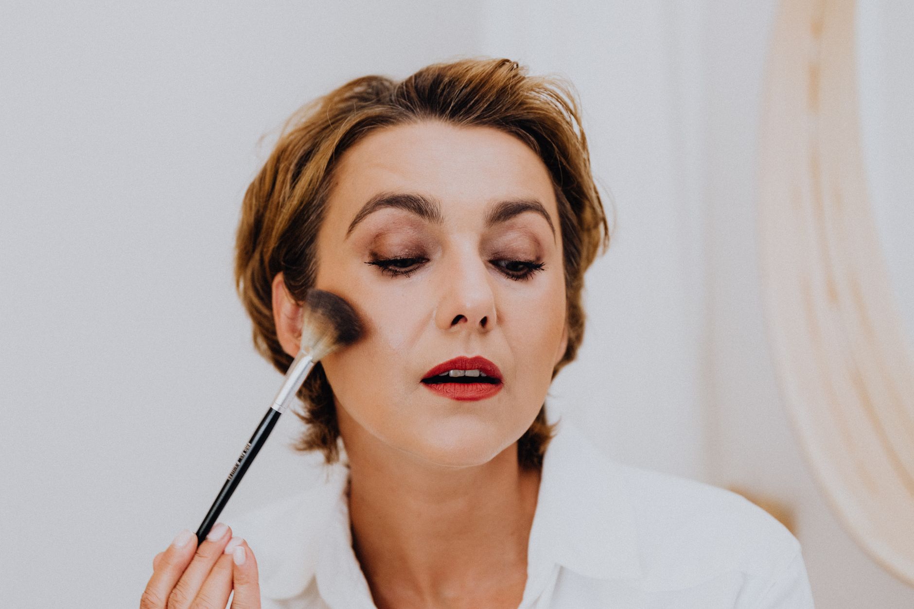 Close-up of an adult woman enhancing her beauty with makeup using a brush, exuding elegance and glamour.