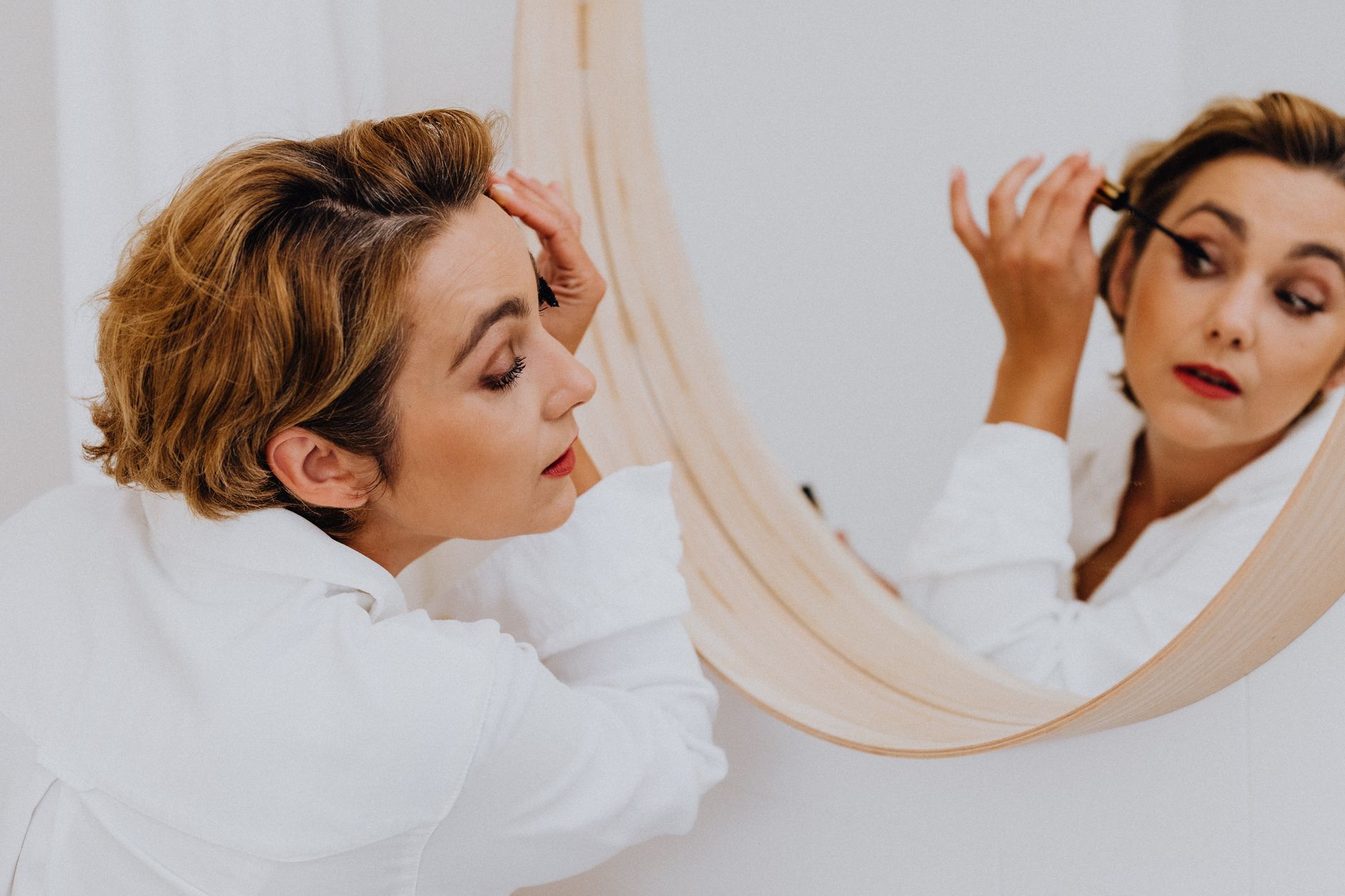 Woman applying mascara in a mirror, showcasing elegance and beauty in a candid indoor setting.