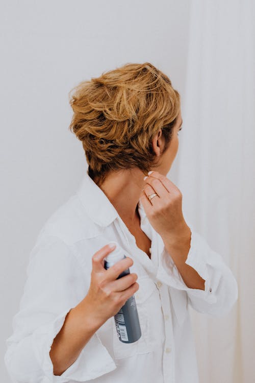Woman in White Long Sleeve Shirt Using Hair Styling Spray