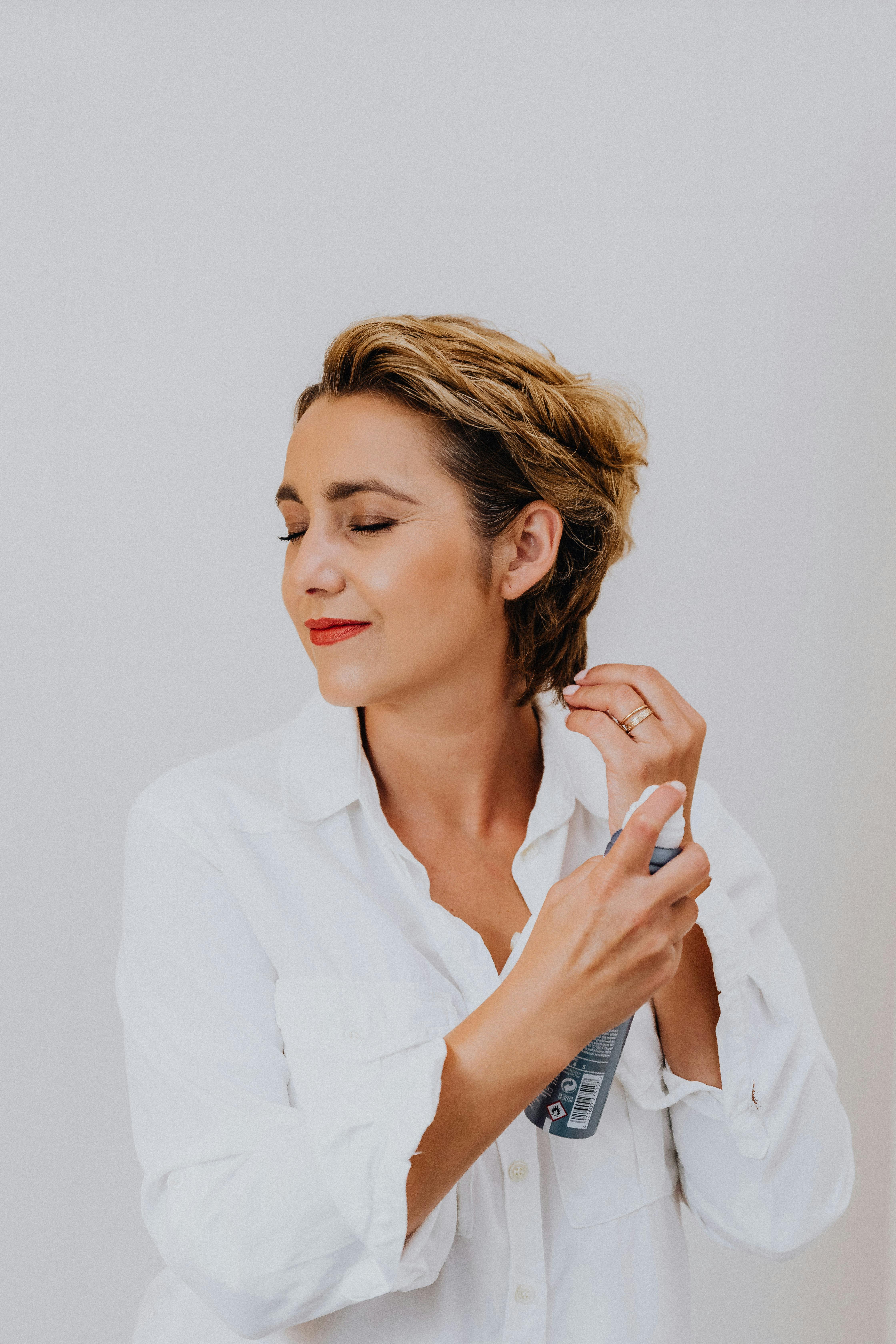 Free Woman in White Long Sleeve Shirt Using Hair Style Spray Stock Photo