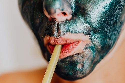 Free Close-up of woman with metallic facial mask sipping through a straw, embodying relaxation and modern skincare. Stock Photo