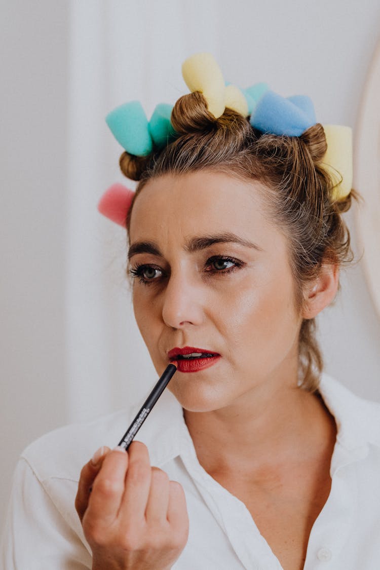 Woman Applying Make Up With Her Hair In Curlers