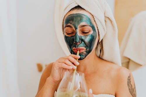 Free Woman with Cosmetic Mask Drinking from a Straw Stock Photo