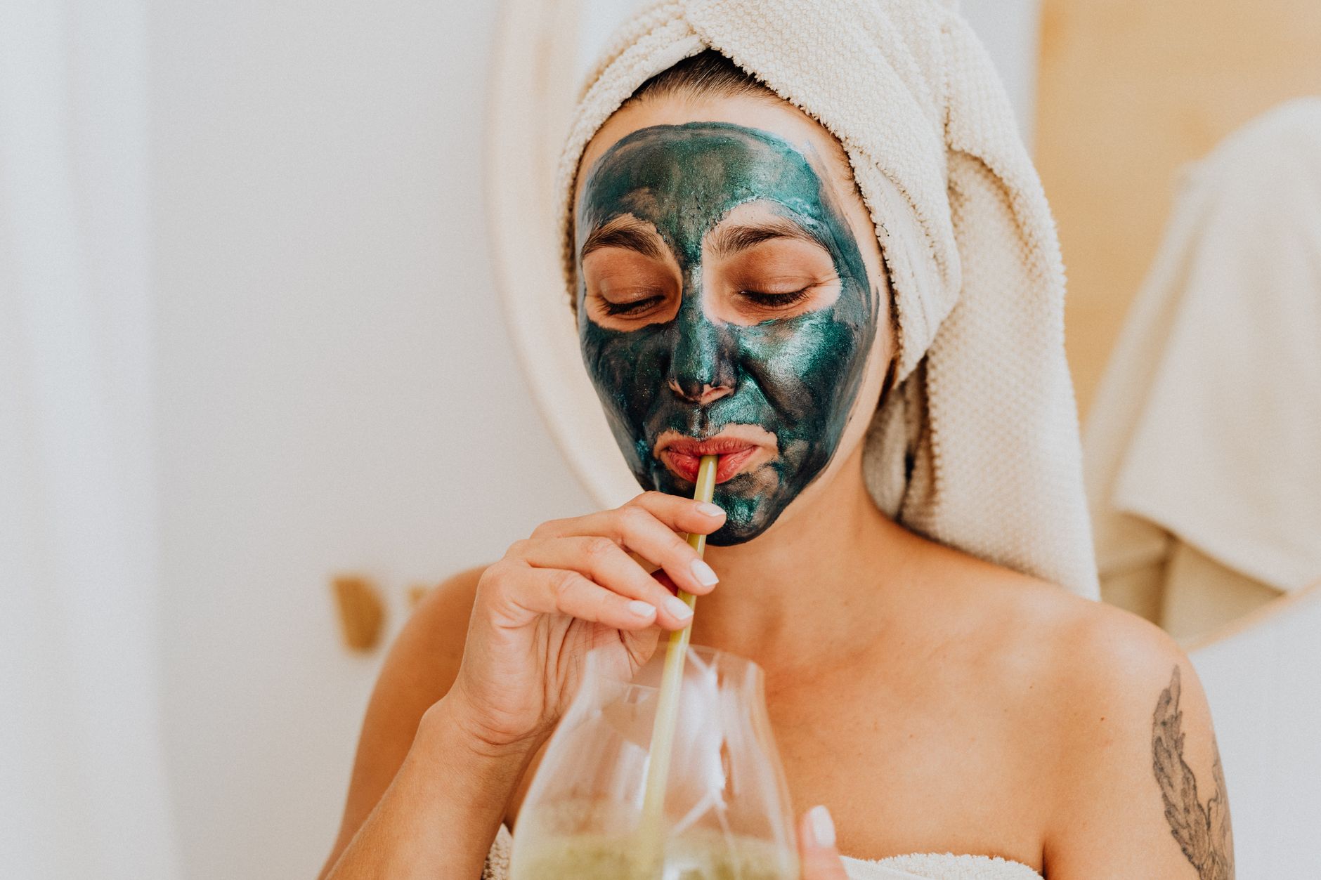 spirulina for spike protein removal women over 50 — Woman enjoying a skincare routine with a face mask and a refreshing drink indoors.
