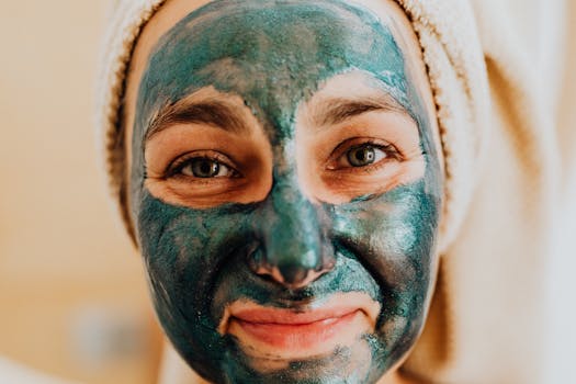 Close-up of a smiling woman with a green face mask, promoting skincare ritual.