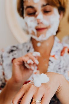 A woman smiles while applying a foaming face mask as part of her skincare routine, creating a fun and self-care moment.