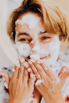 Close-up of a smiling woman with a bubbly face mask emphasizing skincare and self-care.