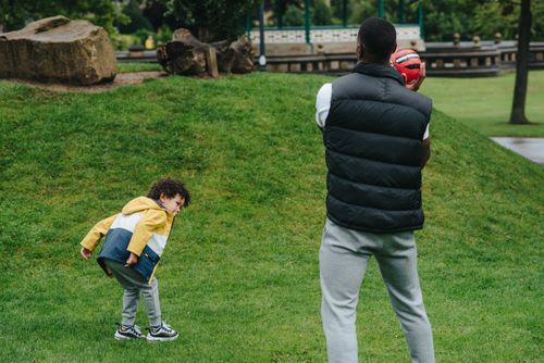 Free Anonymous African American male parent with ball playing with black preschool son while spending time on grassy ground in park Stock Photo