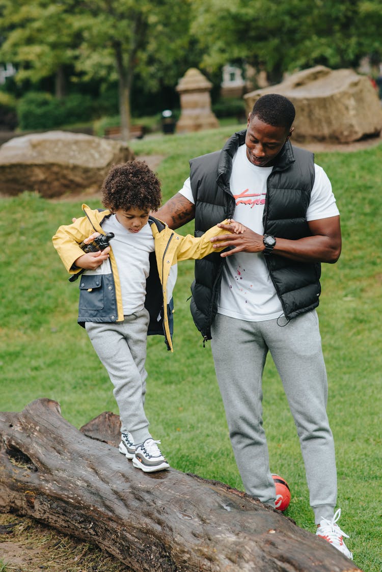 Black Son Walking On Log Near Father